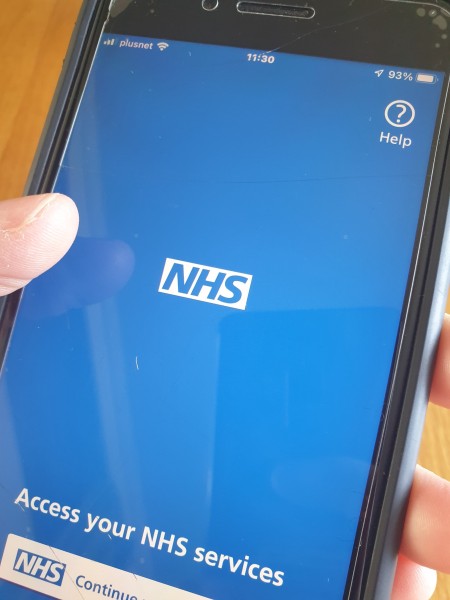 Mobile phone in a hand displaying blue screen and NHS logo